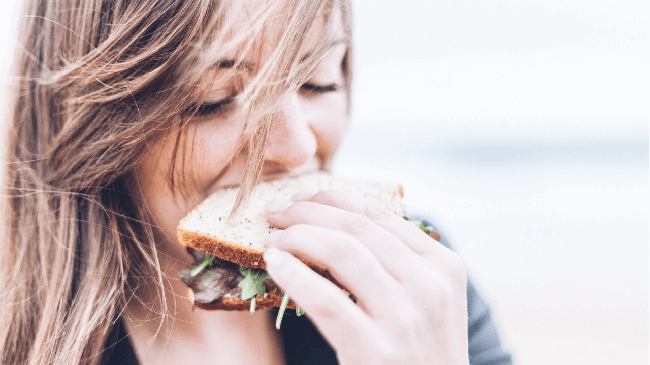 Woman with hair across her face eating a sandwich