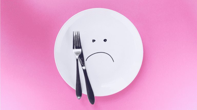 White plate with sad face with silver fork and knife on pink backround