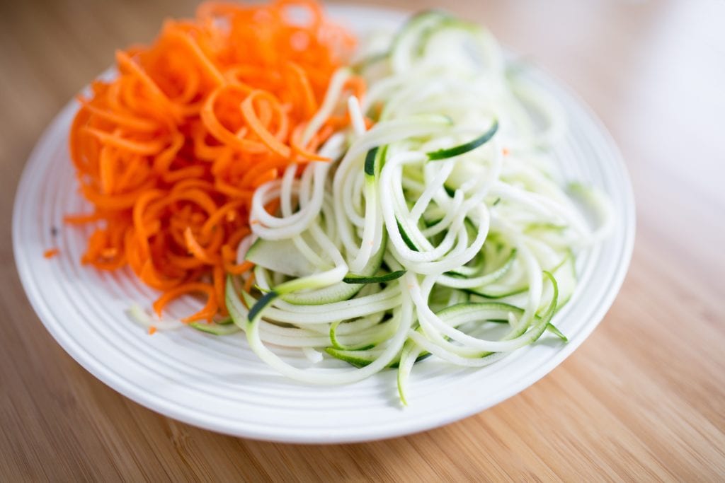 Close up view of white plate on wood table with sliced carrots and cucumbers.