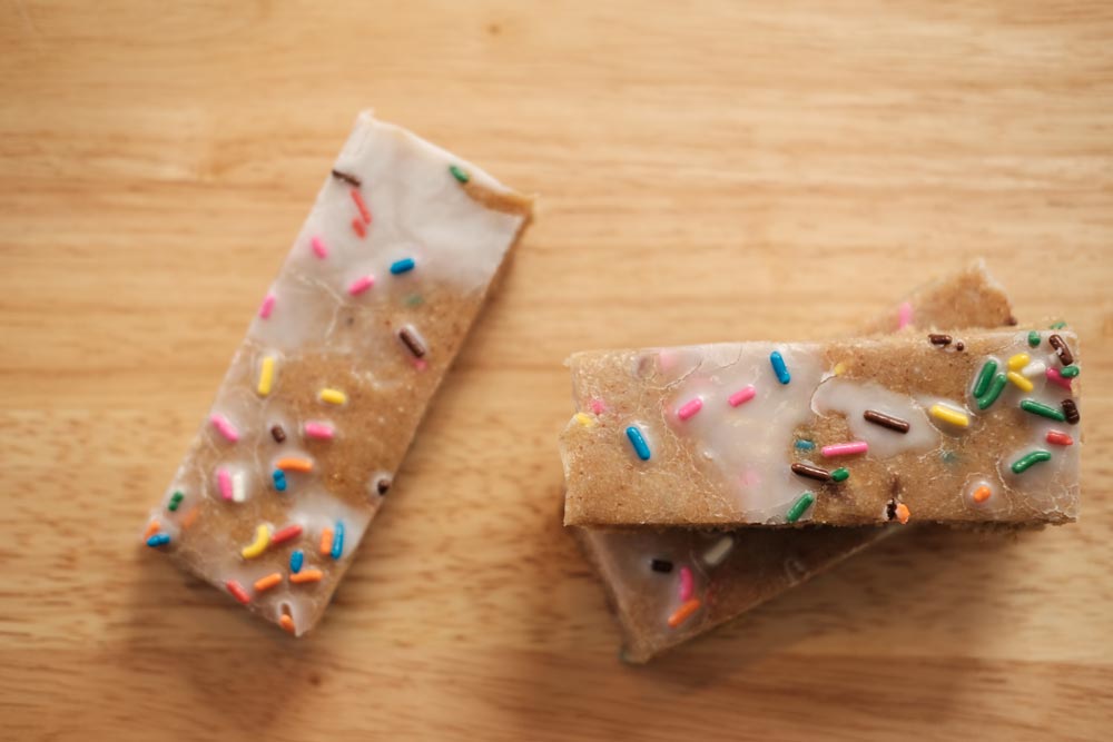 3 protein bars with multi-colored sprinkles on top of light wood table.
