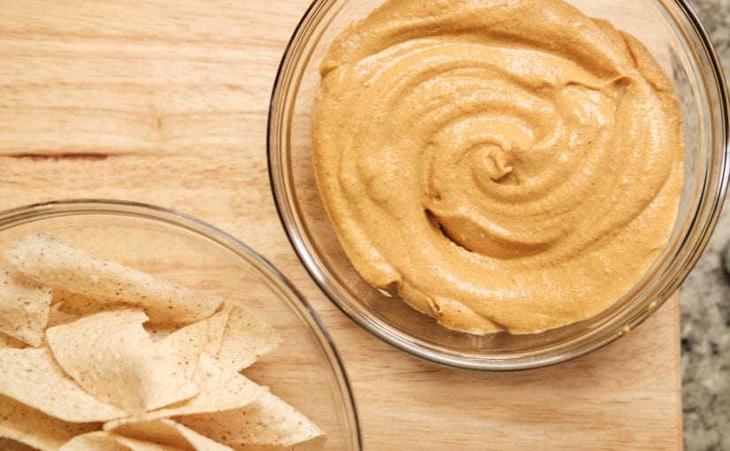 Two clear glass bowls sitting on countertop cutting board one with tortillas chips one with queso cheese.