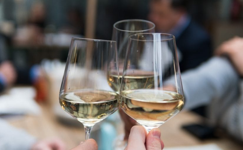 Three wine glasses toasting in restaurant with white wine.