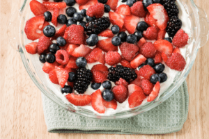 Clear glass bowl of blackberries strawberries blueberries and raspberries in white yogurt.
