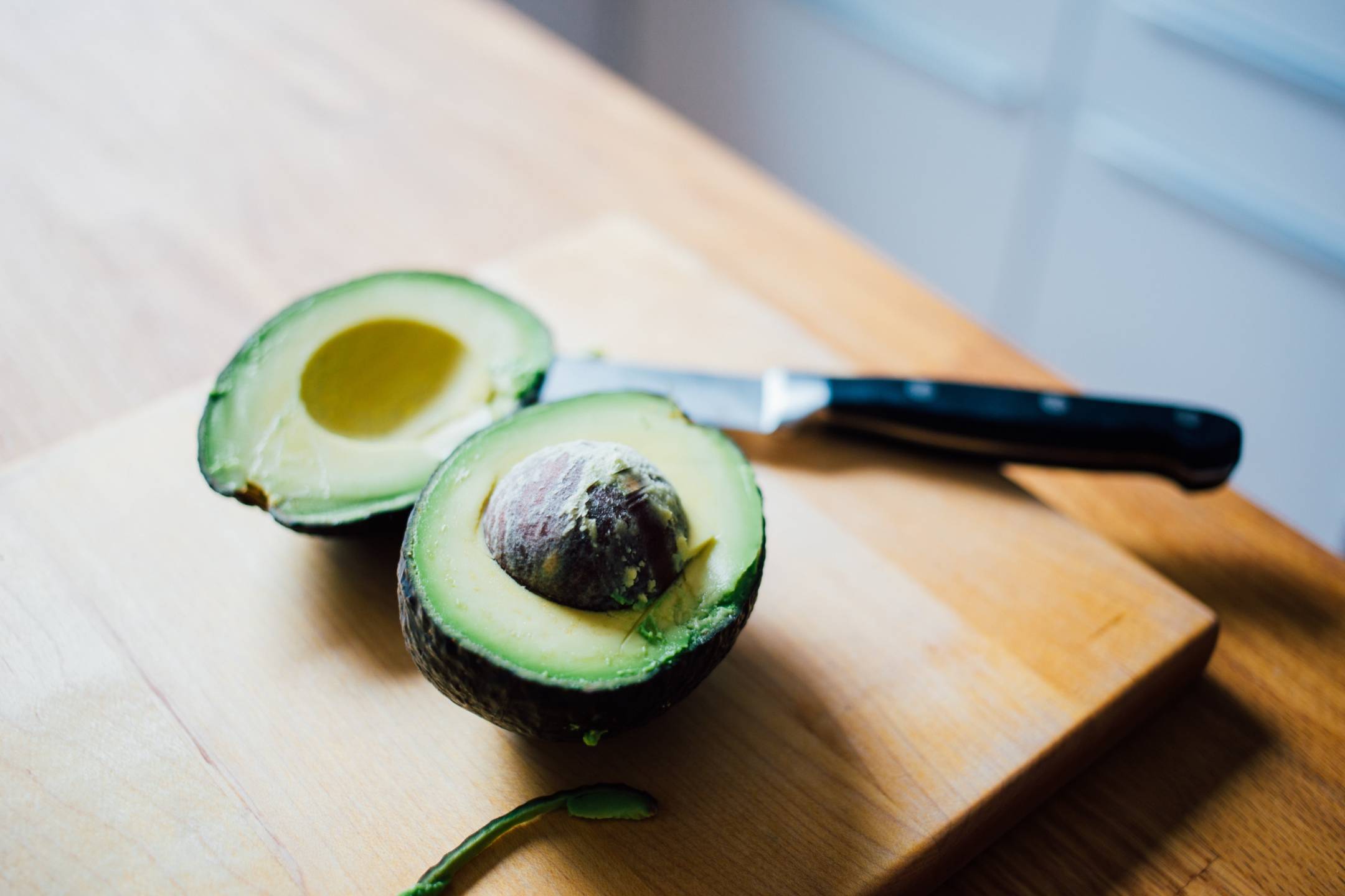 Sliced avocado sitting on top of cutting board with black knife laying next to it.